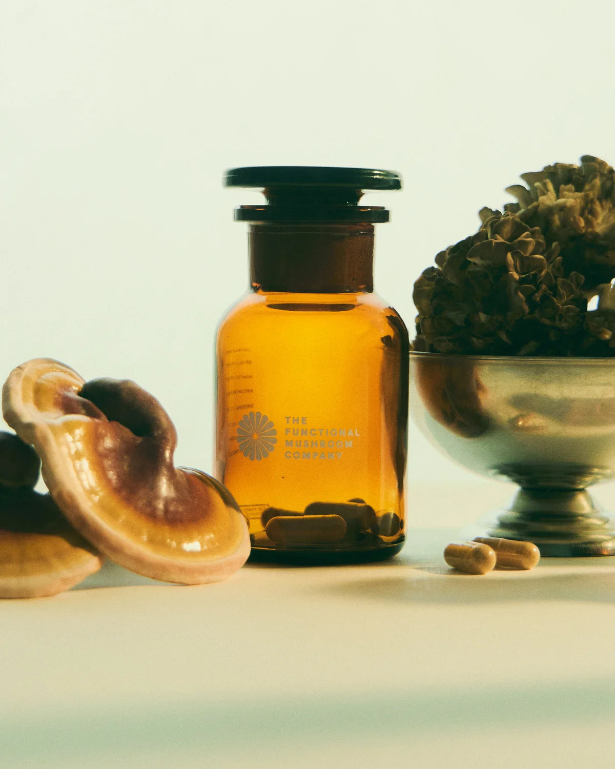 Amber-colored bottle with a black cap on a light background, surrounded by natural elements.