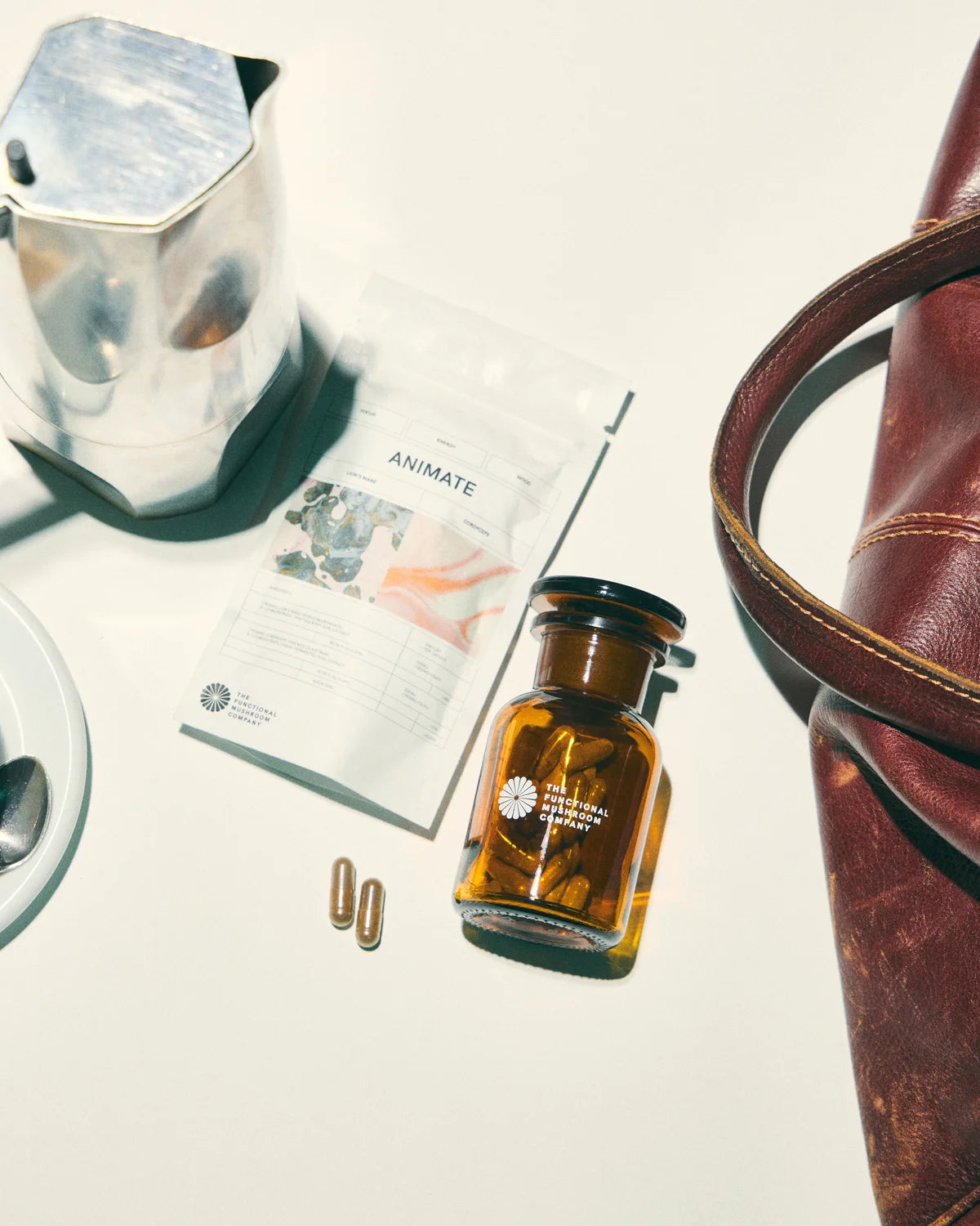 Brown glass bottle with black cap on a white surface with a magazine and leather bag.