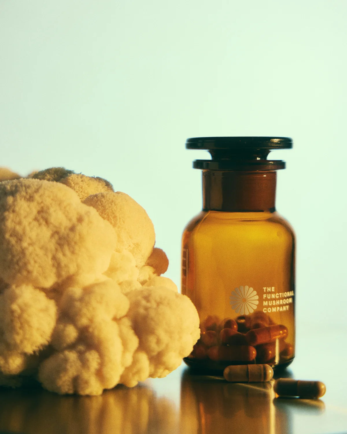 Brown glass bottle with pills next to a cauliflower on a reflective surface