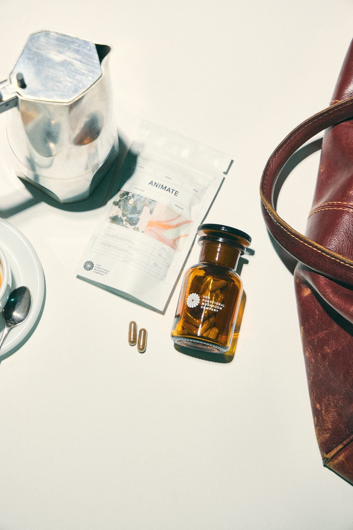 TFMC bottle, refill pouch and capsules beside a coffee pot and bag