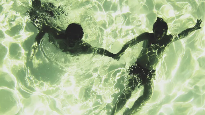 Two swimmers seen from above in bright green water.
